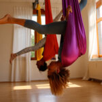 Zwei Frauen hängen kopfüber mit Spagat in Aerial Yoga-Tüchern von der Decke. | Foto: Maarten Hoffmeyer