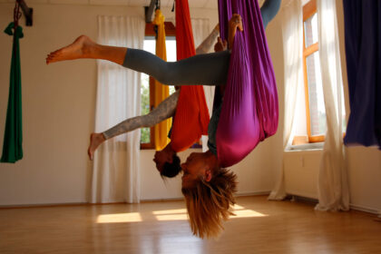 Zwei Frauen hängen kopfüber mit Spagat in Aerial Yoga-Tüchern von der Decke. | Foto: Maarten Hoffmeyer